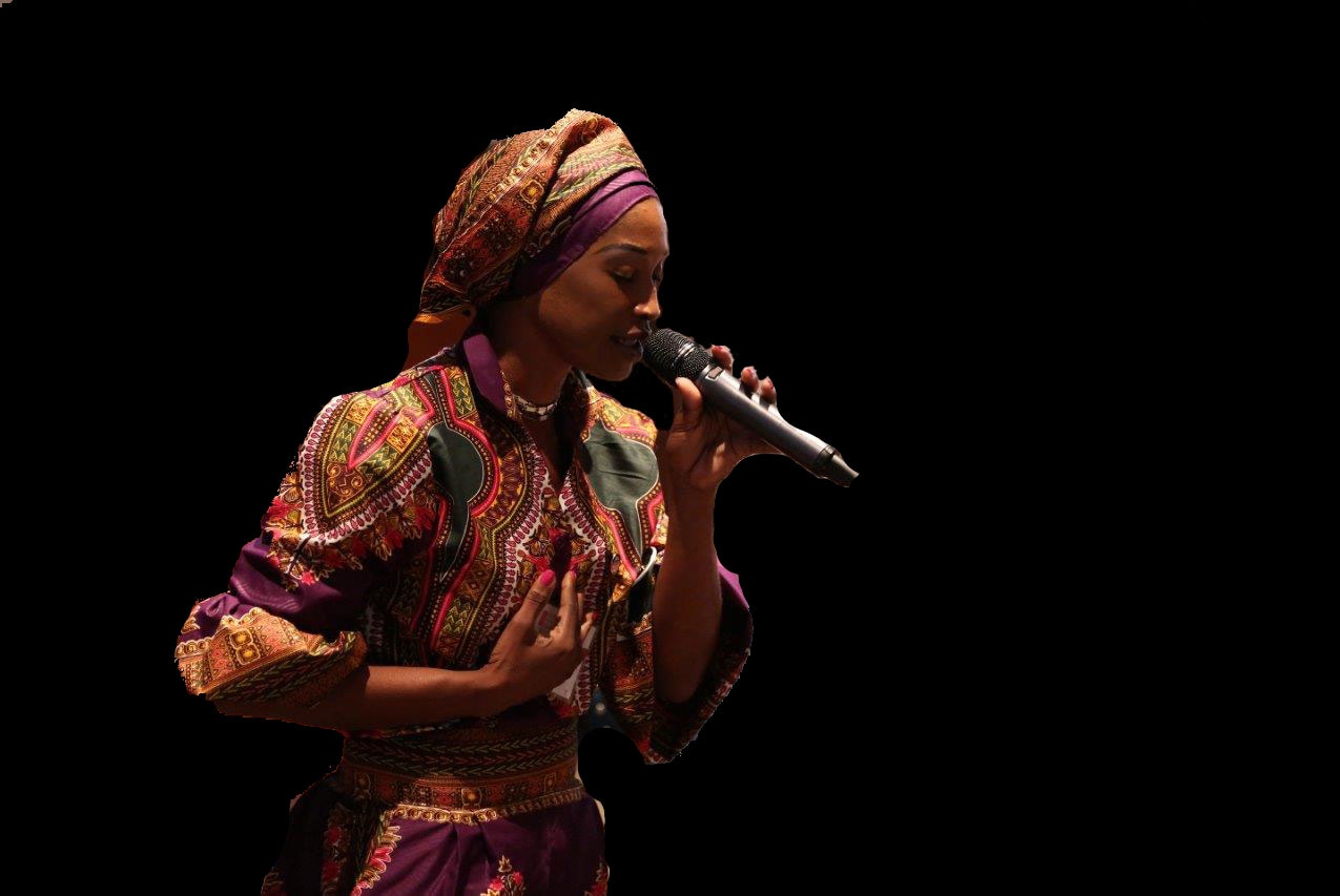 Buki singing on a dark stage in a headwrap